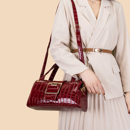 Woman in beige blazer and pleated skirt holding red crocodile texture leather handbag with gold buckle
