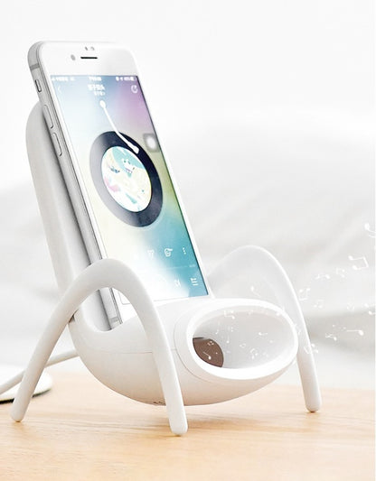 White smartphone playing music on a unique spider-legged speaker dock on a wooden surface