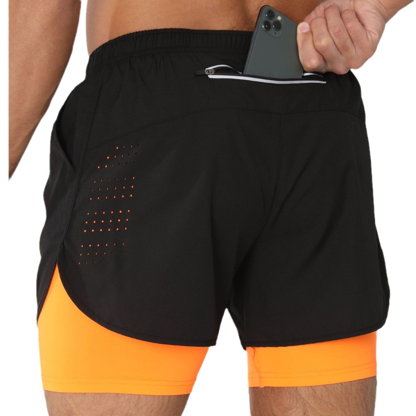 Man wearing black athletic shorts with orange inner lining and back zipper pocket holding phone
