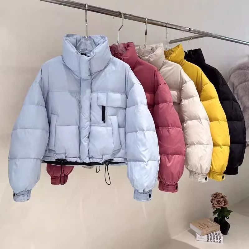Row of cropped puffer jackets in blue, pink, beige, yellow, and black on a metal clothing rack