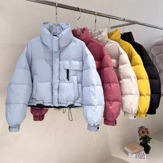 Row of cropped puffer jackets in blue, pink, beige, yellow, and black on a metal clothing rack