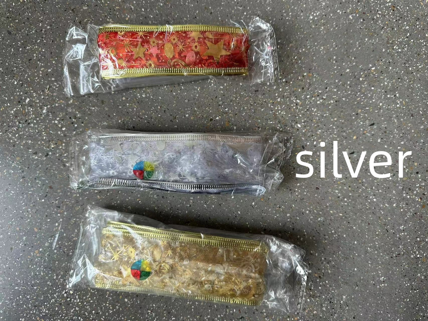 Three decorative ribbon rolls in red, silver, and gold with star patterns, wrapped in clear plastic