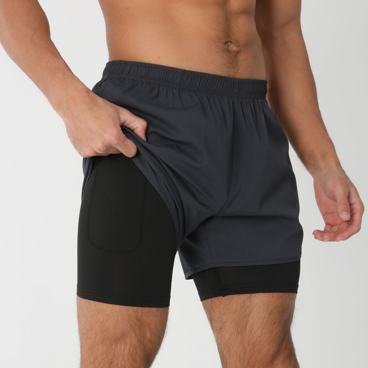 Man showing black inner compression shorts with outer dark gray athletic shorts on white background