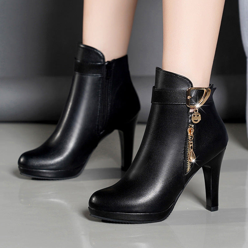 Black high-heeled ankle boots with side zipper and gold buckle detail on a smooth floor