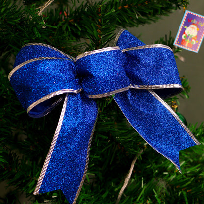 Sparkling blue glitter Christmas bow with silver edges on green pine tree branch