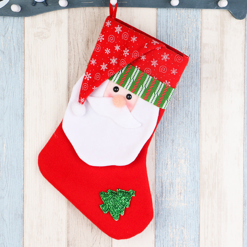 Red Christmas stocking with Santa face, green striped hat, and glittery green tree on wood background