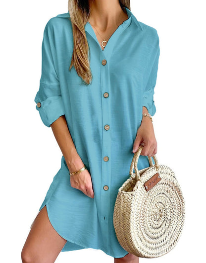 Woman wearing relaxed light blue button-up shirt dress with rolled sleeves, holding a round woven straw handbag