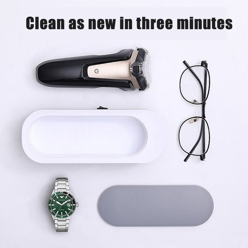 Electric shaver, cleaning station, eyeglasses, wristwatch, and gray case on white surface