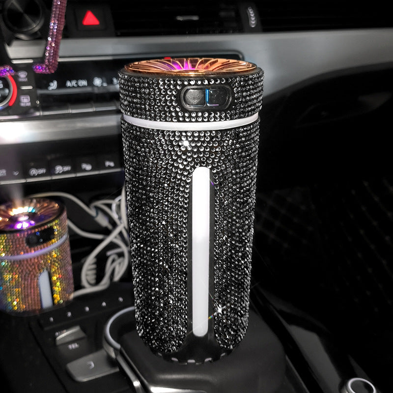 Black rhinestone-covered portable car air purifier plugged into a car's center console with glowing top