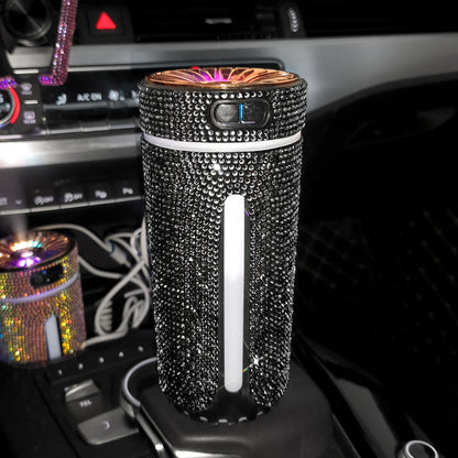 Black rhinestone-covered portable car air purifier plugged into a car's center console with glowing top