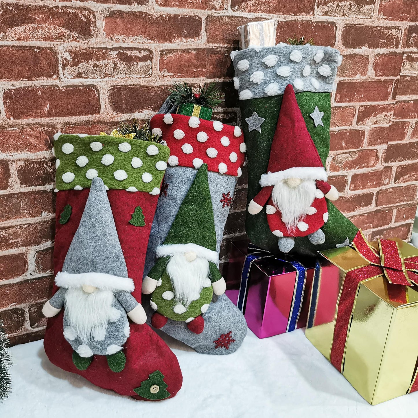 Three festive Christmas stockings with gnome decorations beside wrapped gift boxes on a white surface