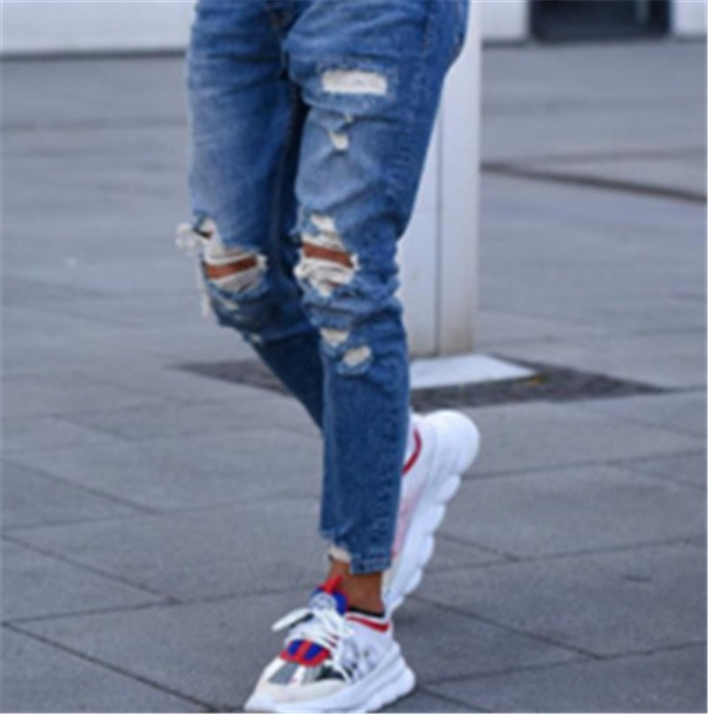 Person wearing distressed blue jeans and modern white sneakers with red and blue accents on city pavement