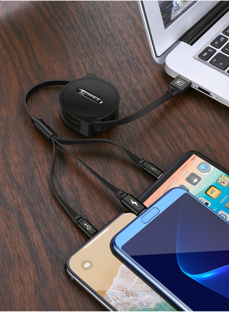 Retractable multi-device charging cable connected to laptop and charging three smartphones on wooden surface