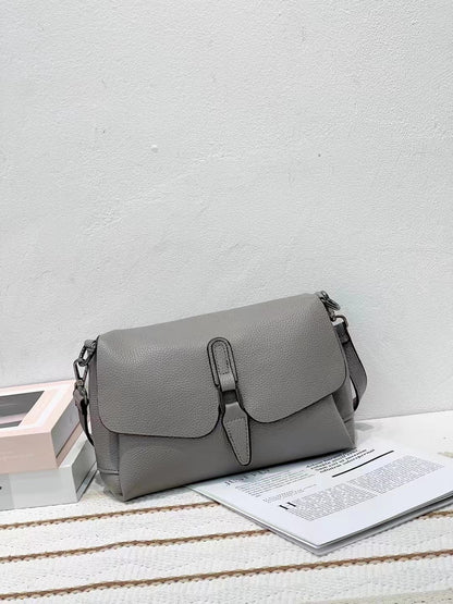 Gray leather crossbody handbag on striped fabric with open magazine and stacked books