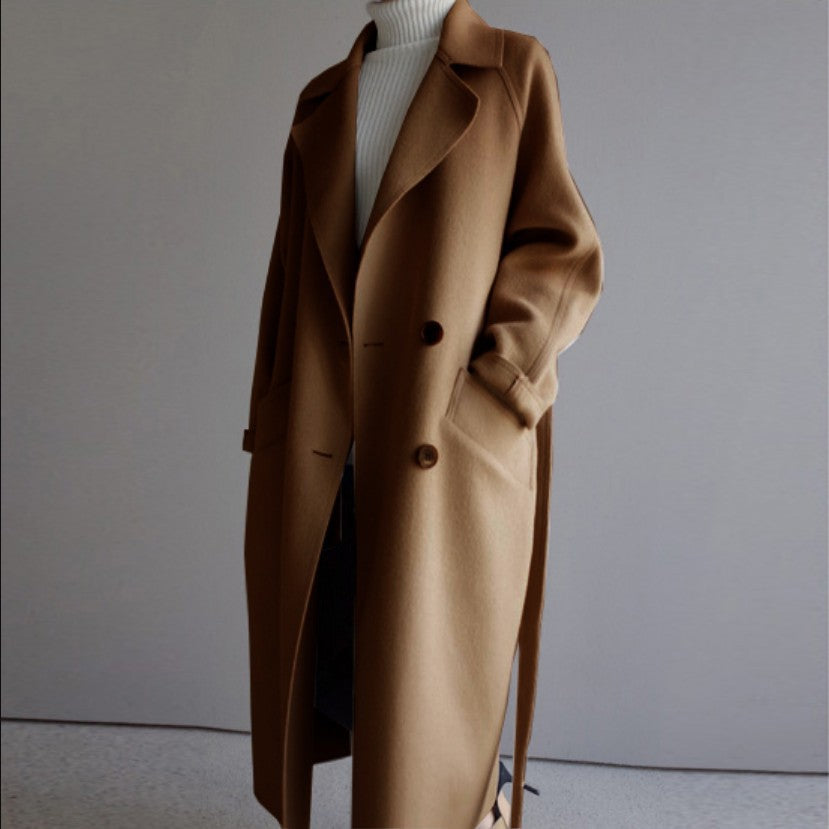 Long camel brown wool coat with buttons over white turtleneck sweater in minimal indoor setting