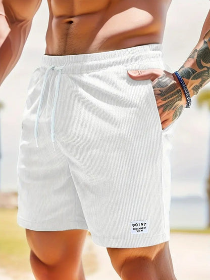 Close-up of muscular man wearing white ribbed shorts with drawstring and tattooed hand in pocket on beach