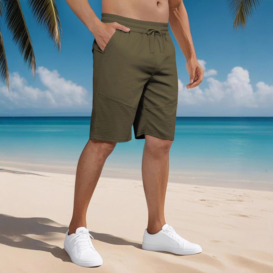 Man wearing olive green casual shorts and white sneakers on a tropical beach with blue ocean