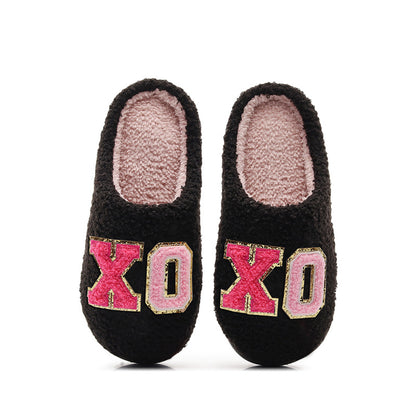 Black fuzzy slippers with pink plush lining and 'XO' embroidered in red and pink letters