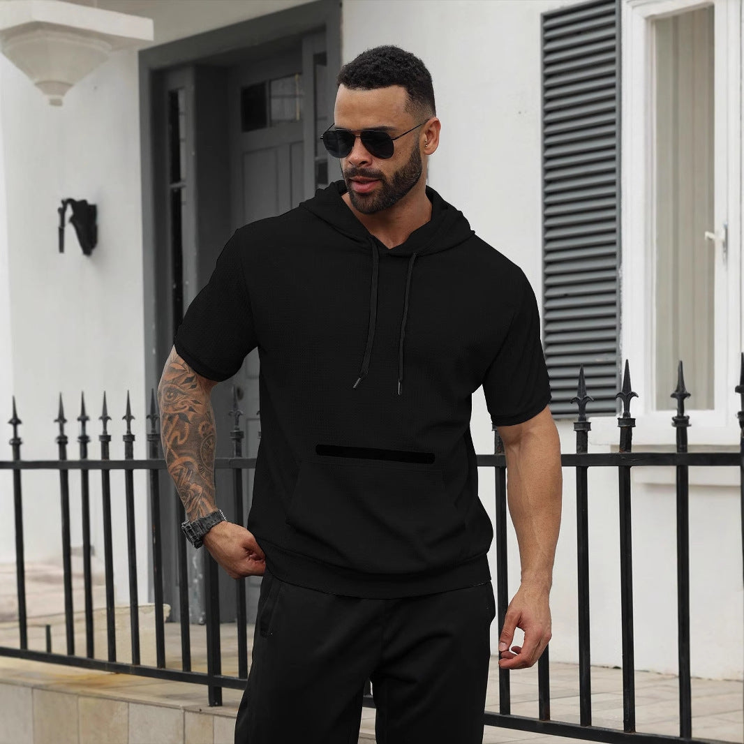 Man with tattooed arm wearing black short-sleeve hoodie and sunglasses near black fence