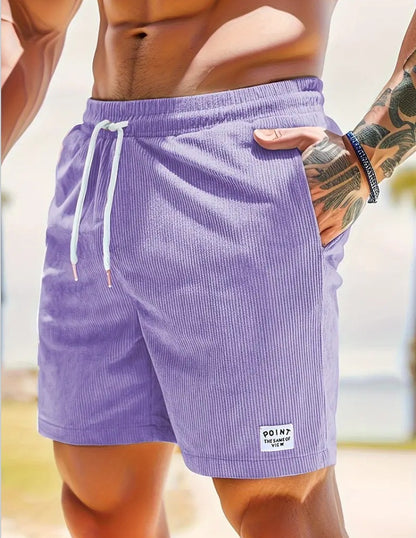Close-up of a muscular man wearing purple corduroy shorts with white drawstrings and tattooed arm