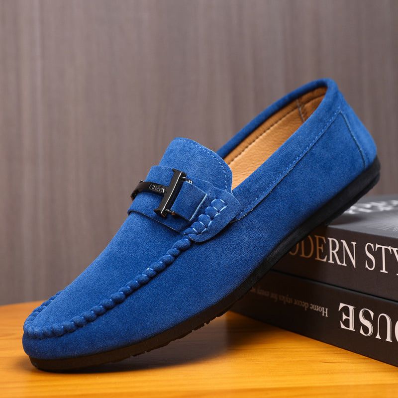 Blue suede men's loafer with black metal buckle on wooden surface against brown background