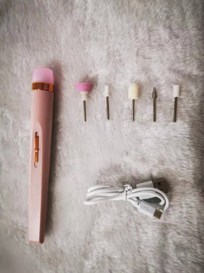 Pink electric nail drill kit with six metal and foam drill bits and a white USB charging cable on gray fabric