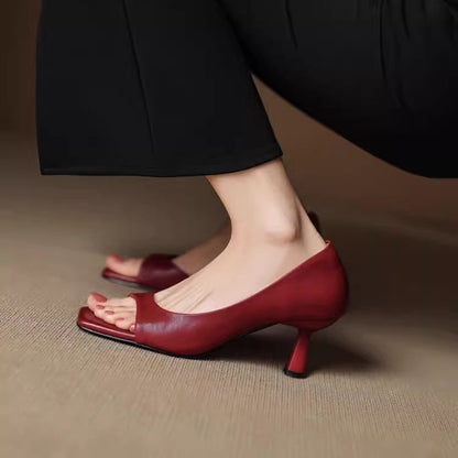 Close-up of feet wearing red low heel open-toe leather shoes with black pants on beige floor
