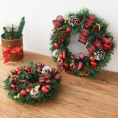 Two festive Christmas wreaths decorated with pinecones, red berries, tartan ribbons, and red ornaments on a wooden surface
