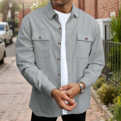 Man wearing a gray textured button-up shirt over a white t-shirt with watch and ring, standing outdoors