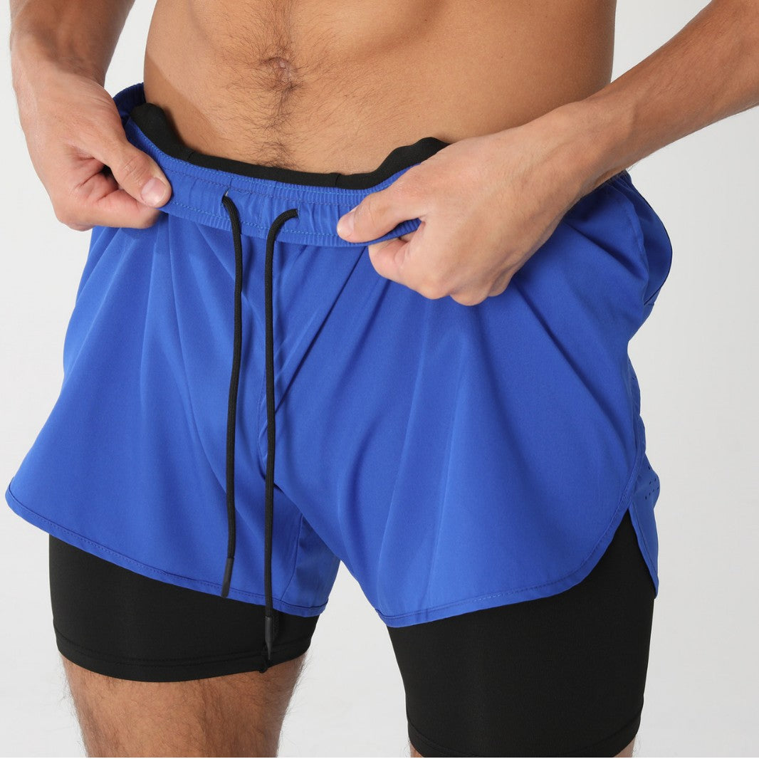 Close-up of a man adjusting royal blue athletic shorts over black compression leggings against light background