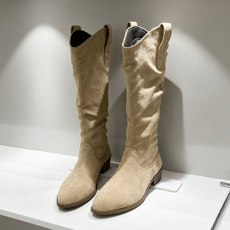 Pair of beige suede knee-high boots with low block heels on white display shelf