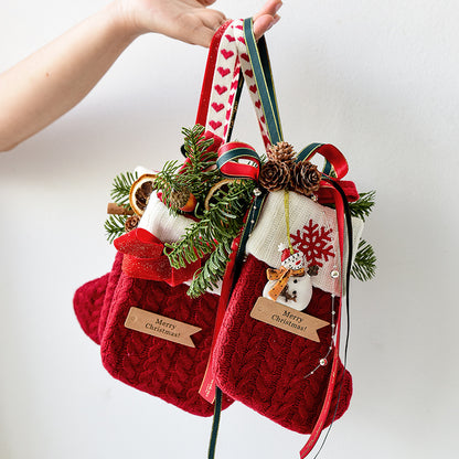 Hand holding two red knitted Christmas stockings decorated with pine cones, greenery, ribbons, and snowman ornaments
