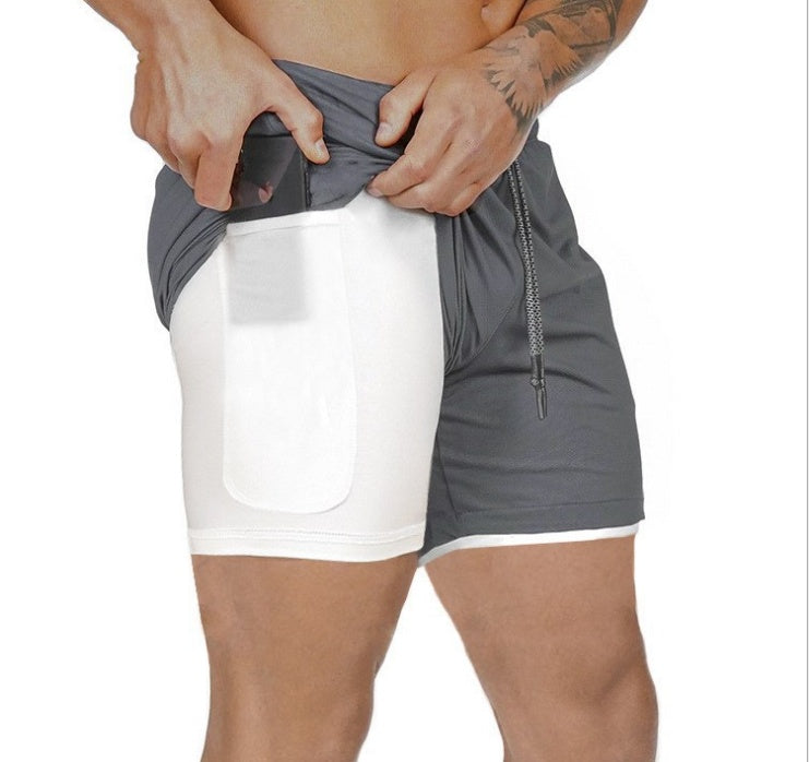 Man wearing gray athletic shorts with built-in white compression pocket holding a smartphone