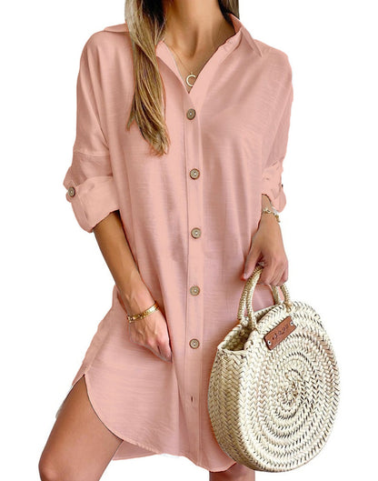 Woman wearing light pink button-up shirt dress with rolled sleeves holding round woven straw handbag