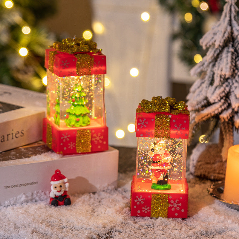 Christmas-themed snow globes with Santa and tree inside red glittery gift boxes on snowy surface with warm lights