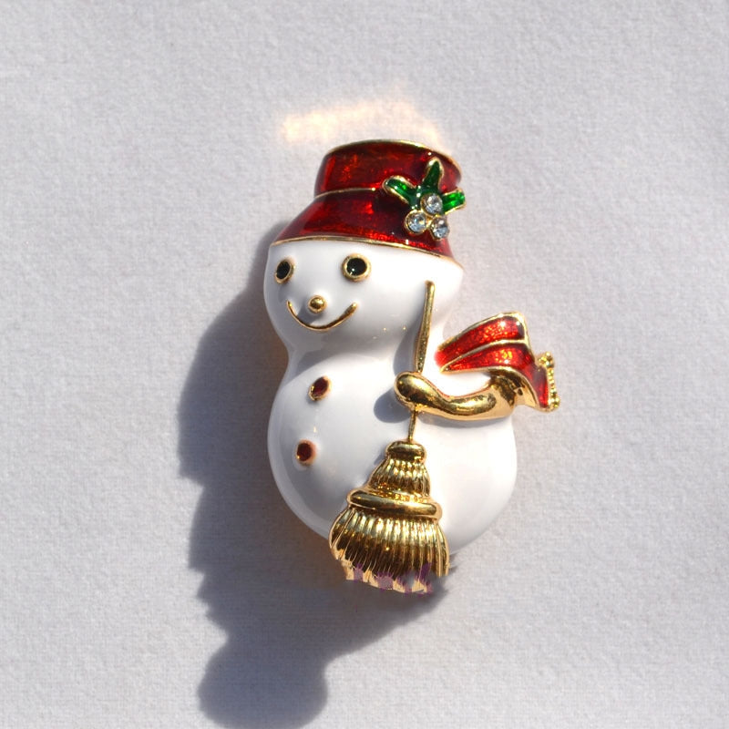 Christmas snowman brooch with red hat, scarf, and golden broom on white background