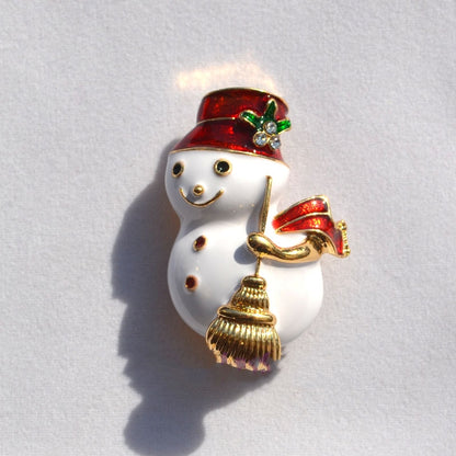 Christmas snowman brooch with red hat, scarf, and golden broom on white background