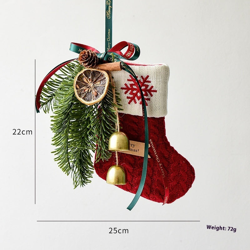 Red and white Christmas stocking ornament decorated with pine branches, dried orange slice, pinecone, cinnamon stick, gold bells, and ribbons