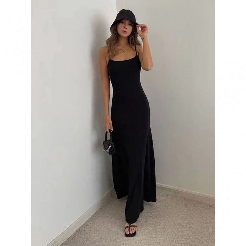 Woman wearing a black maxi dress, bucket hat, holding a small black handbag, posing indoors