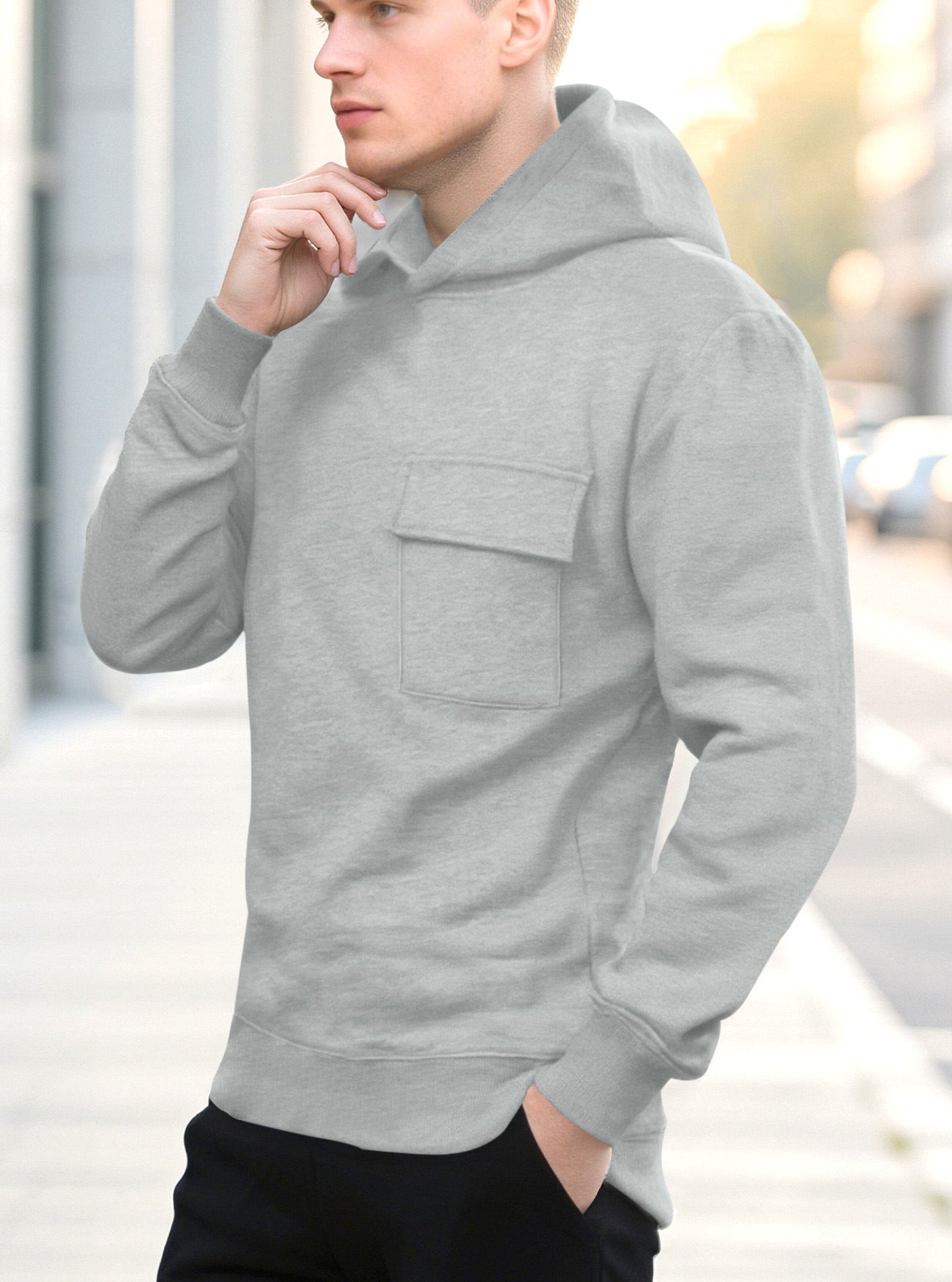 Young man wearing light gray hoodie with chest pocket, posing on city sidewalk at sunset