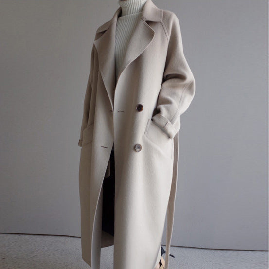 Long beige wool trench coat over white turtleneck sweater, minimalist indoor setting