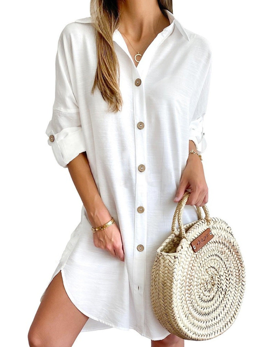 Woman wearing a white button-down shirt dress with rolled sleeves, holding a round woven straw handbag
