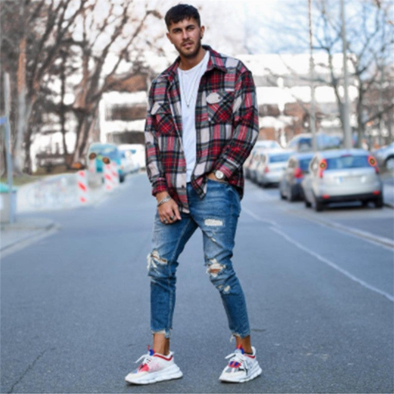 Young man wearing red plaid shirt, white t-shirt, ripped blue jeans, and white sneakers standing on urban street