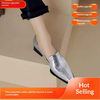 Silver leather women's shoe with low block heel, worn with black cuffed pants, beige background