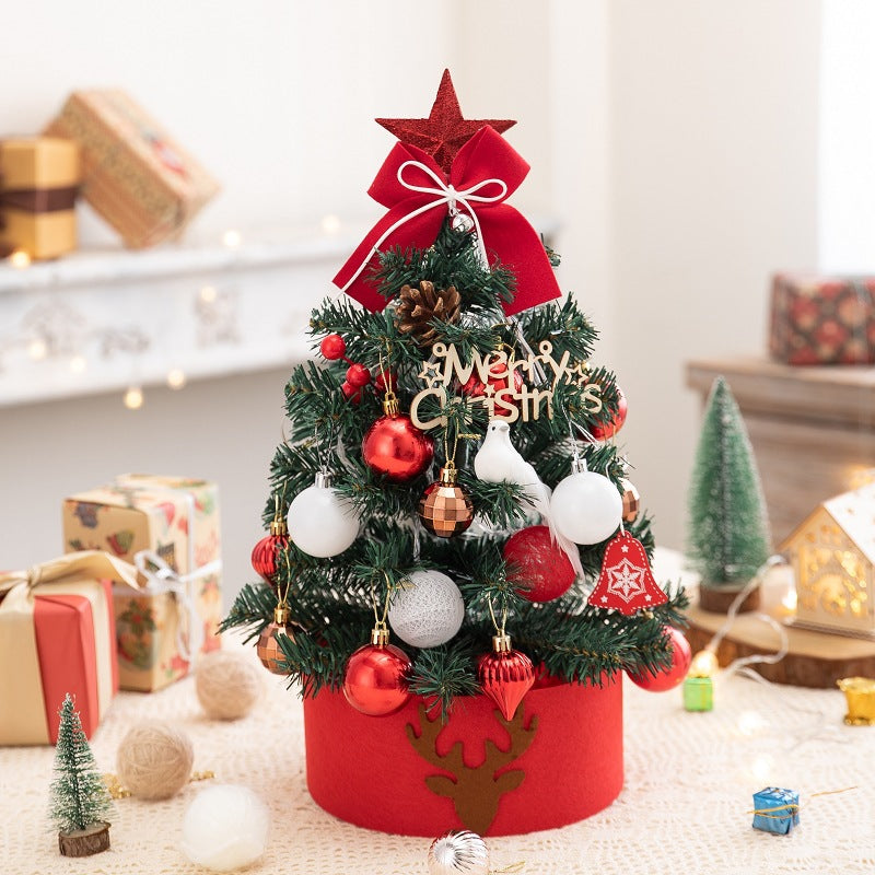 Small decorated Christmas tree with red bow, ornaments, pinecone, and Merry Christmas sign on table with gifts
