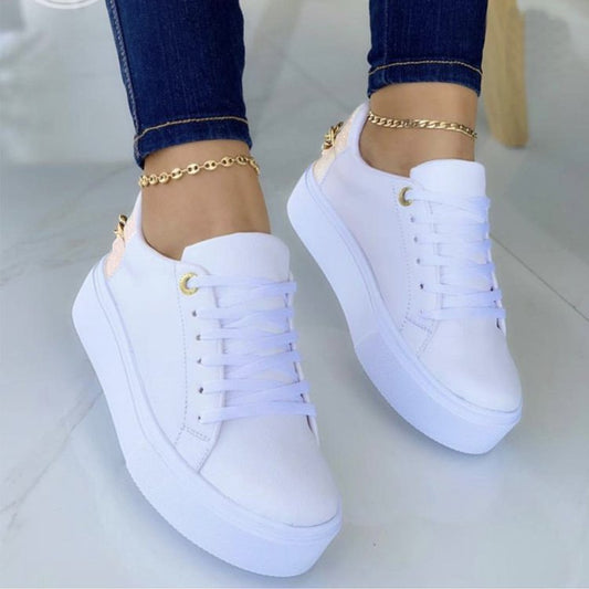 White platform sneakers with gold eyelets and accents worn with dark blue jeans and gold anklets on a light floor