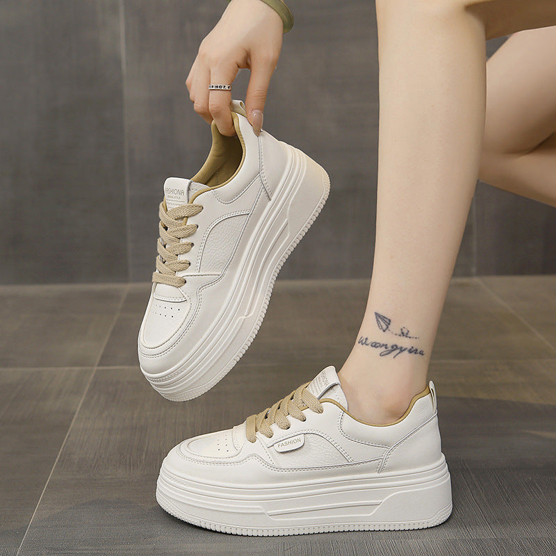 Platform white sneakers with beige laces worn by person with ankle tattoo on gray tiled floor