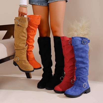 Woman wearing black knee-high boots standing next to red and blue boots, holding brown and orange boots