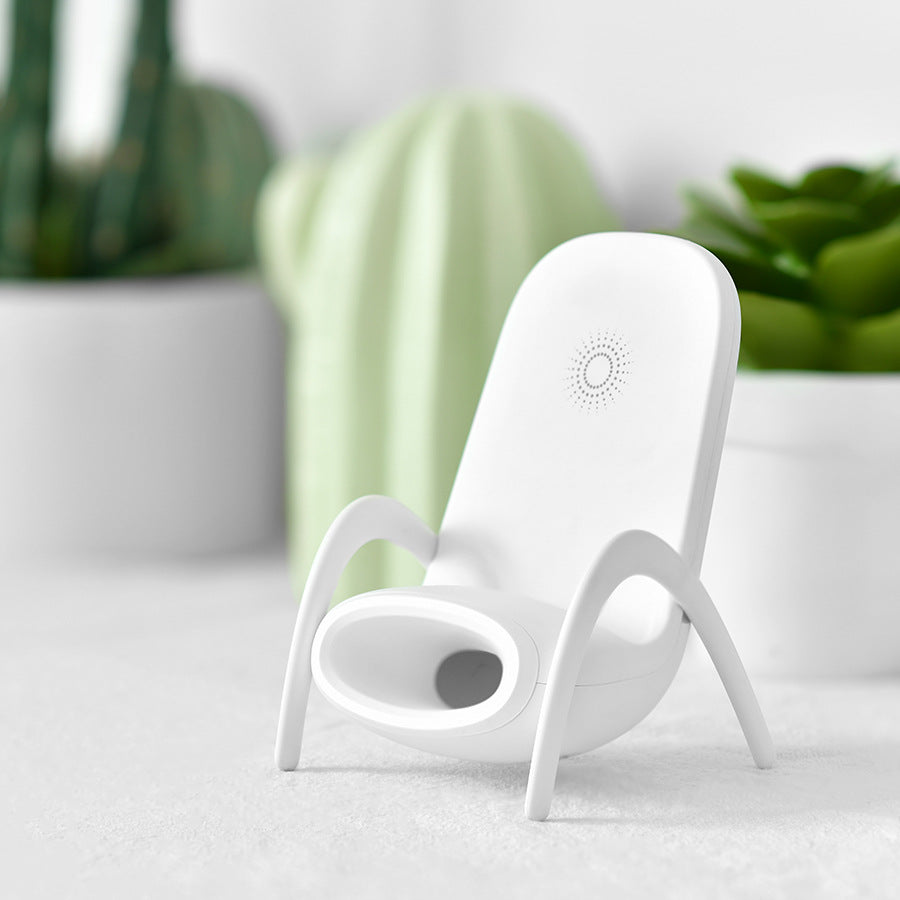 White modern device holder with curved legs on white surface, green succulents in background