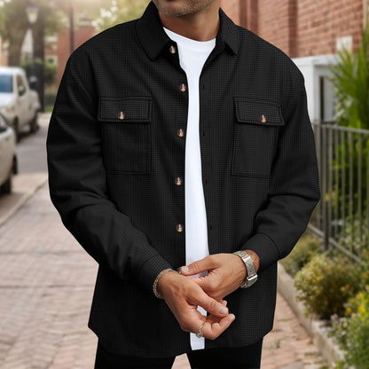 Man wearing a black textured button-up shirt over a white t-shirt, standing on a cobblestone street